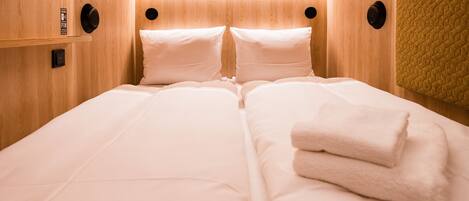 Cama doble con sábanas blancas y una toalla doblada, paredes de paneles de madera y una pared texturizada a la derecha.