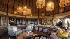 Un hall espacioso con techo alto, lámparas colgantes de mimbre y diversos arreglos de asientos, incluyendo sofás y sillones.