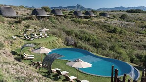 Un resort con cabañas de techo de paja, piscina y sillones de descanso.