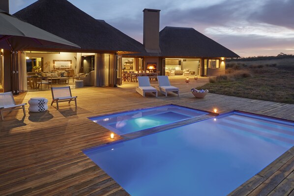 A poolside area with lounge chairs, a wooden deck, and a building with an open design.