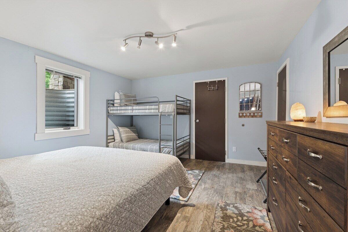 Une chambre avec des lits superposés, une commode, un miroir et une fenêtre avec des stores.