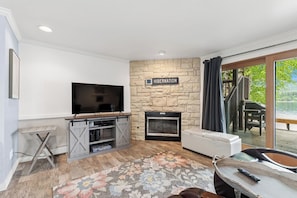 A living room with a stone wall, a fireplace, a flat-screen TV, and a view to the outside.