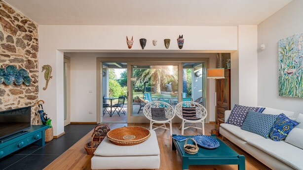 Una sala de estar con pared de piedra, televisor, sofá y comedor con sillas y mesa.