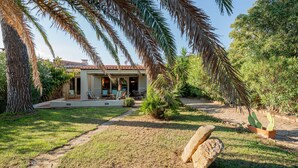 Una casa con porche cubierto, mobiliario exterior y un jardín con palmeras y cactus.