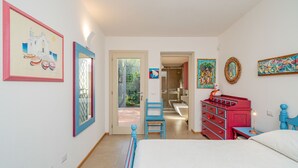 Un dormitorio con cama, cómoda y silla. Hay una puerta que da al baño.