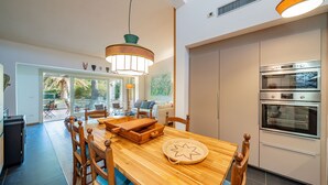 Una cocina moderna con hornos integrados, un comedor con muebles de madera y vistas al exterior.