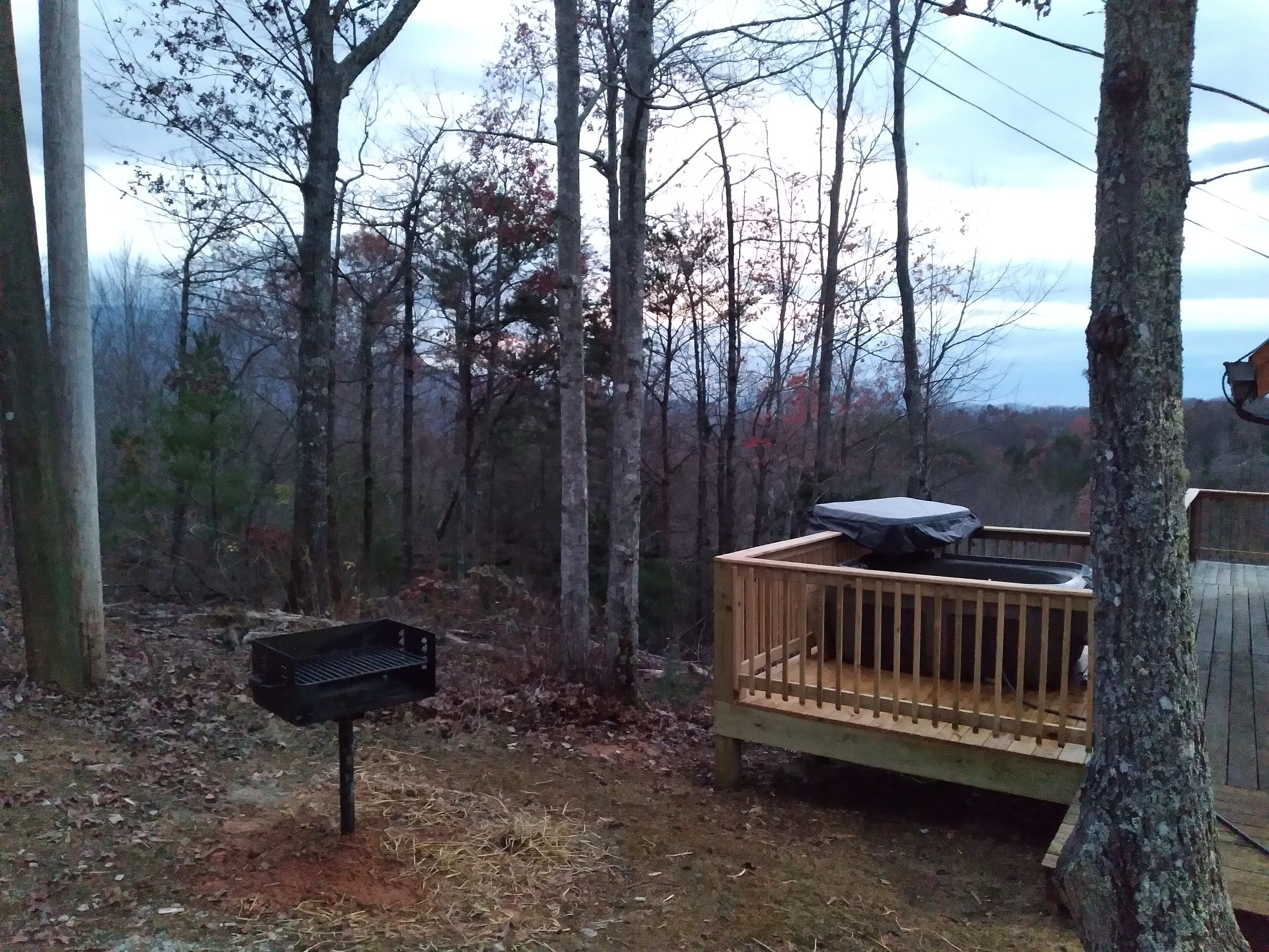 Une terrasse en bois avec un barbecue et un espace abrité, entourée d’arbres dans une zone boisée.