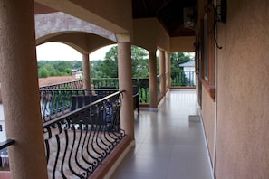 A covered balcony with a tiled floor and a wrought iron railing.