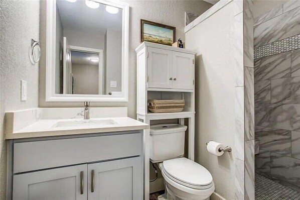 Un baño con un lavamanos blanco, espejo y inodoro, además de una zona de ducha con azulejos de mármol.