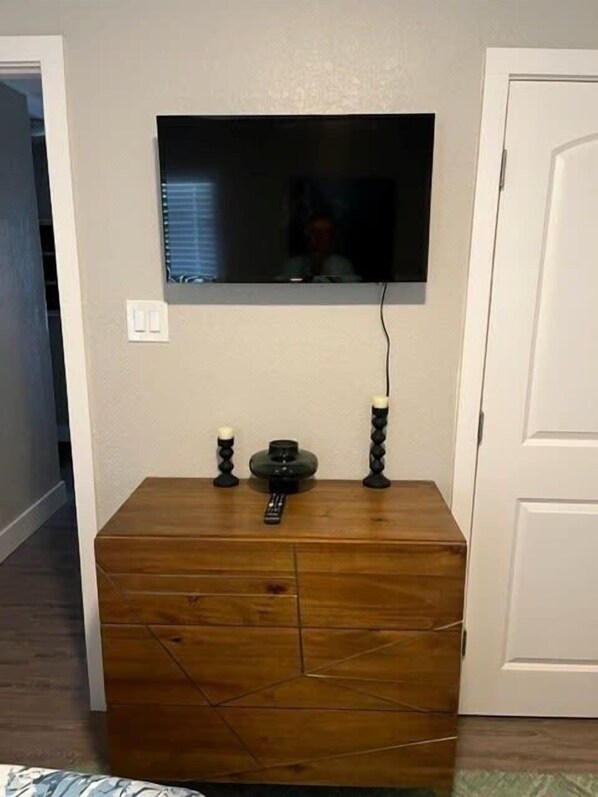 Una habitación con un televisor montado en la pared, un mueble de madera debajo y una puerta a la derecha.