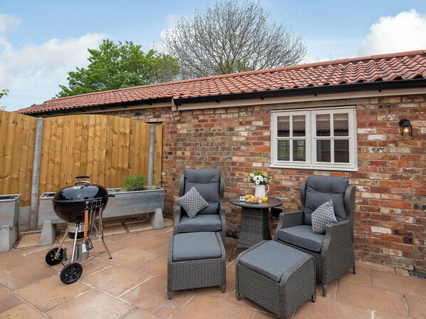A patio with wicker furniture, a barbecue, and a brick wall with a window.