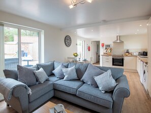 A modern living room with a grey sectional sofa, a dining area, and a kitchen with white cabinets and appliances.