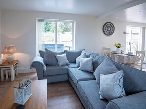 A modern living room with a grey sectional sofa, a small table with a lamp, and a dining area with a table set for two.