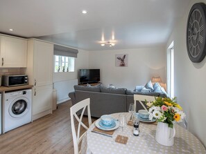 Un espacio habitable compacto con kitchenette, un sofá, una mesa de comedor con un florero y un reloj de pared.