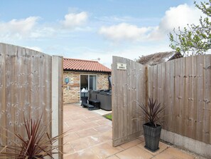 Une porte en bois donnant sur un patio équipé d’un jacuzzi et bordé d’un mur en briques.