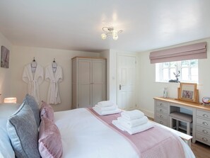 A bedroom with a bed, bedside tables, a wardrobe, a vanity with a mirror, and a window with a view.