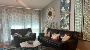 A living room with a black leather sofa, a coffee table, and a ceiling fan. - Island Dunes Condo's-#1307-One block from beach (Port Aransas)