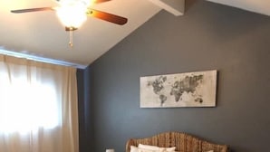 A bedroom with a large bed, two bedside tables, a ceiling fan, and a world map on the wall. - Island Dunes Condo's-#1307-One block from beach (Port Aransas)