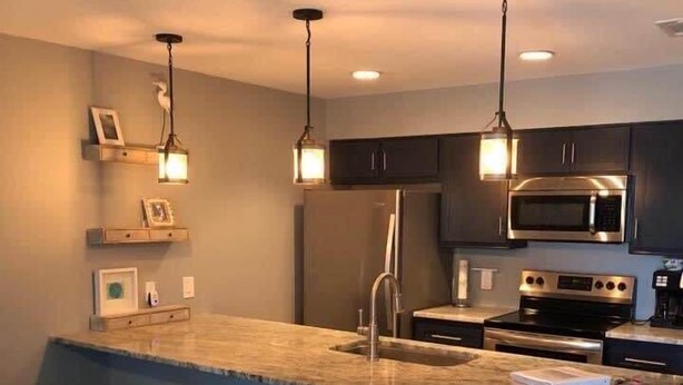 A modern kitchen with dark cabinets, stainless steel appliances, and pendant lighting. - Island Dunes Condo's-#1307-One block from beach (Port Aransas)