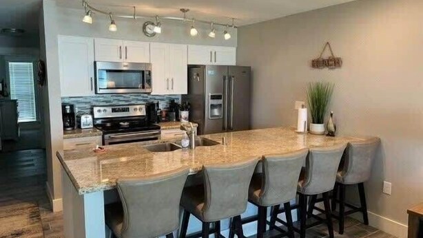 A modern kitchen with granite countertops, stainless steel appliances, and a central island with bar stools. - One Block from Beach-Pelicans Landing! - Unit 1405 - Island Dunes Condo's (Port Aransas)