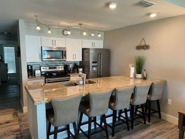 A modern kitchen with granite countertops, stainless steel appliances, and a central island with bar stools.