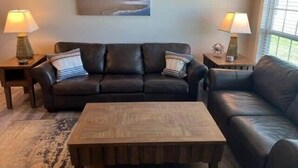 A living room with a sofa, a coffee table, two lamps, and a painting on the wall. - One Block from Beach-Pelicans Landing! - Unit 1405 - Island Dunes Condo's (Port Aransas)
