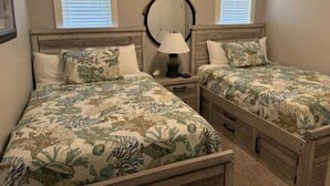 A bedroom with two beds, a nightstand, a mirror, and a window with blinds. - One Block from Beach-Pelicans Landing! - Unit 1405 - Island Dunes Condo's (Port Aransas)