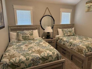 A bedroom with two beds, a nightstand, a mirror, and a window with blinds.