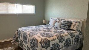 Un dormitorio con cama, mesita de noche, lámpara y ventana con persianas.