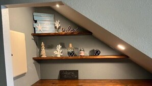 Una escalera de madera con escalones que conducen a un rellano con un estante que contiene objetos decorativos y un letrero.