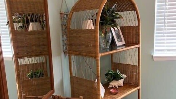 Een kamer met een grote spiegel, een rieten plank met planten en een kleine houten stoel.