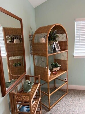 Una habitación con un espejo grande, una estantería de mimbre con plantas y una pequeña mesa de madera.
