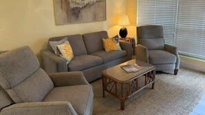 Een woonkamer met een bank, fauteuils, een salontafel en een lamp.
