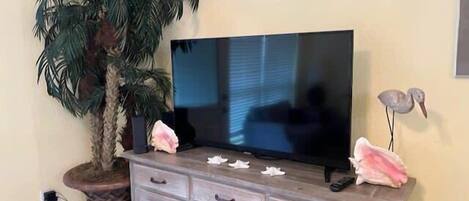 A television on a wooden cabinet with drawers, a potted plant, and decorative items.