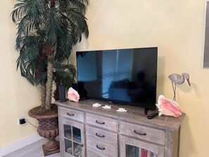 Un téléviseur posé sur un meuble en bois doté de tiroirs, une plante en pot et des objets décoratifs.