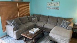 A living room with a sectional sofa, a wooden coffee table, and a ceiling fan. - Crabb Shack-One block from Beach-Island Dunes Condo's-#1606 (Port Aransas)