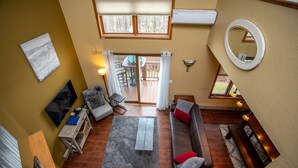 A living room with a sofa, armchair, coffee table, TV, and a view of the outdoors through a sliding door.