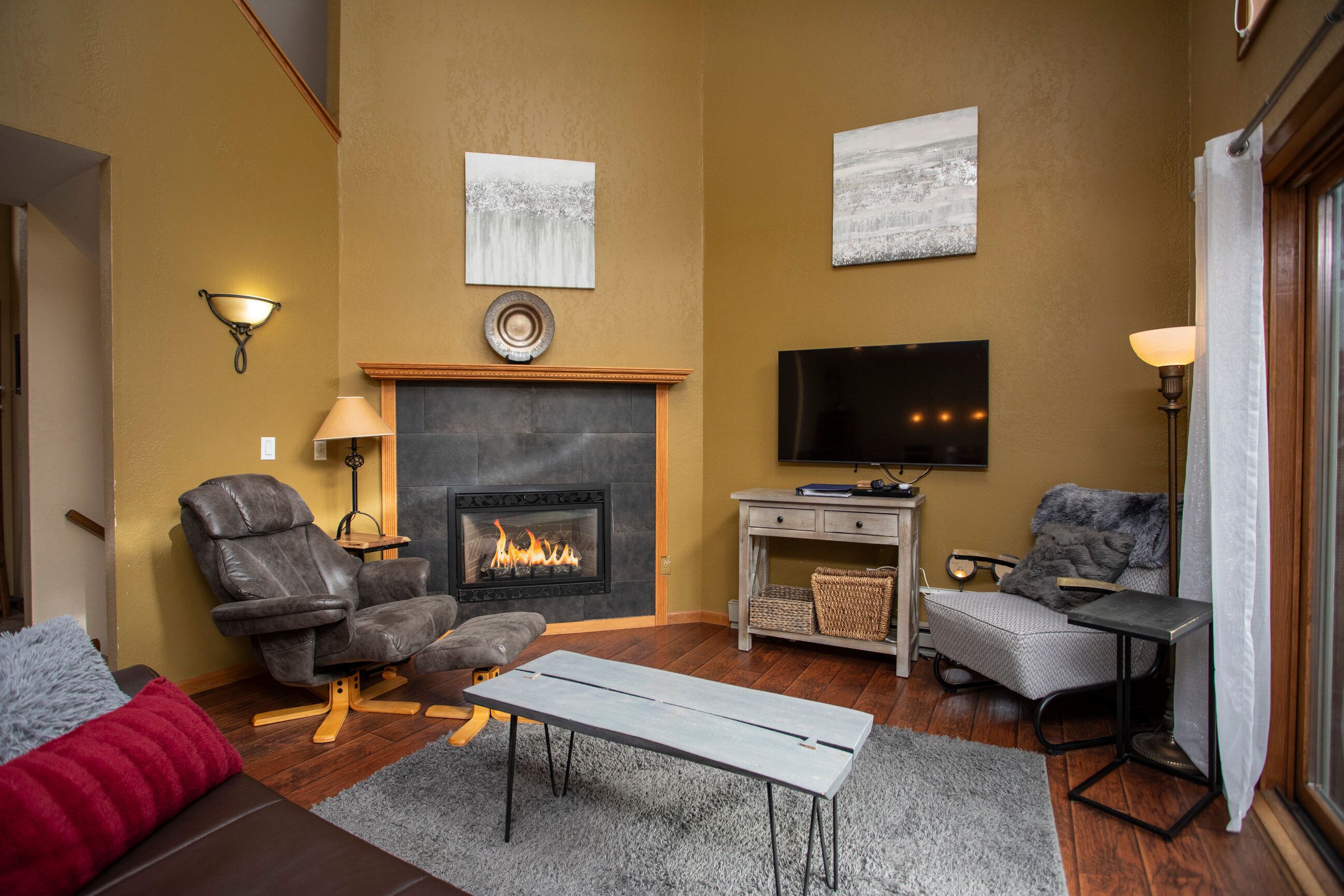 A living room with a fireplace, leather chairs, a sofa, a flat-screen TV, and a small table.