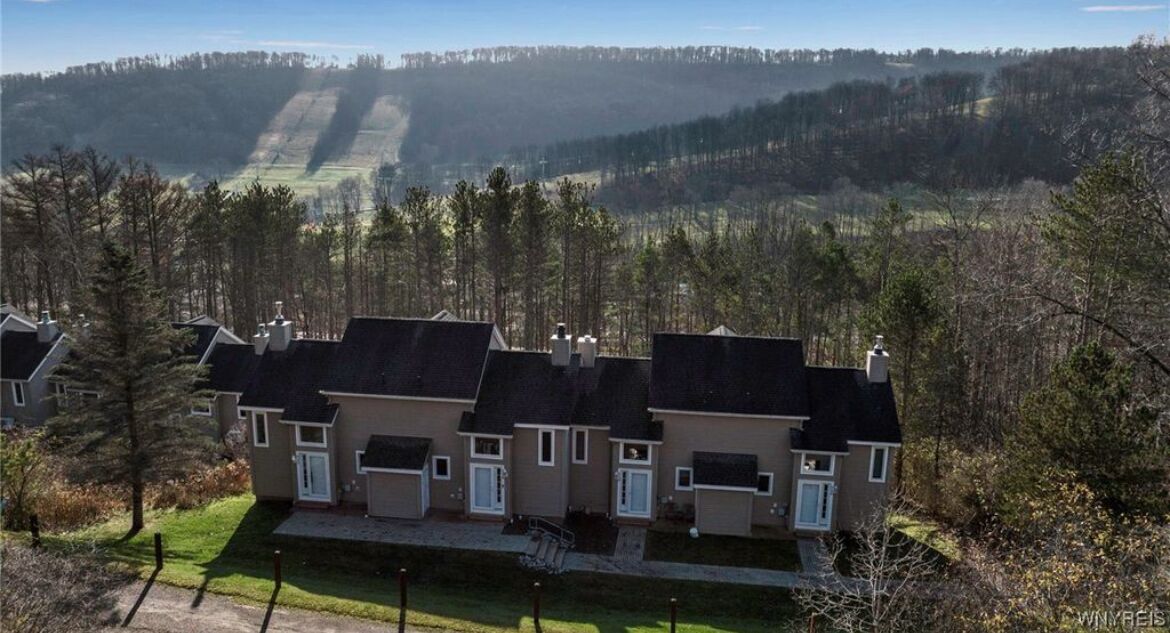 A row of modern houses with a sloped roof, surrounded by a forested landscape.