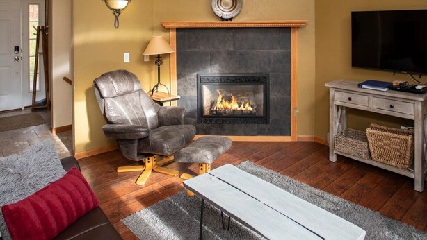 A living room with a fireplace, a sofa, a coffee table, a television, and a ceiling fan.