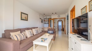 Una sala de estar con sofá, mesa de centro, televisor y una zona de comedor al fondo.