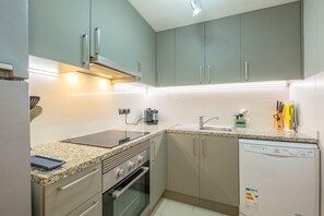 A modern kitchen with grey cabinets, a built-in oven, a dishwasher, and a granite countertop.