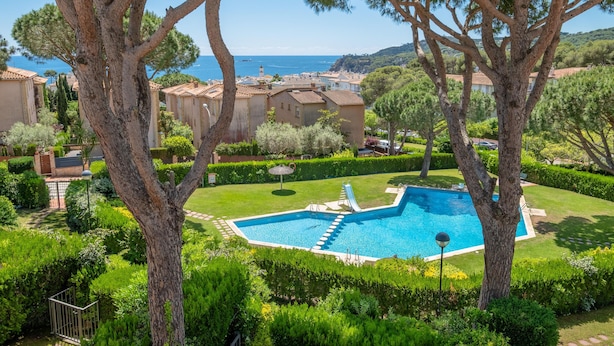 Una piscina rodeada de abundante vegetación y edificios de estilo mediterráneo.