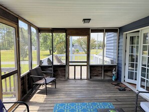 A covered porch with a bench, a table, and a view of a house and trees. - Shucker's Tump -  pet friendly, Lg screened porch. LINENS AND TOWELS PROVIDED (Chincoteague)