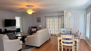 A living room with a ceiling fan, a TV, a sofa, a dining table with chairs, and a window with blinds. - Shucker's Tump -  pet friendly, Lg screened porch. LINENS AND TOWELS PROVIDED (Chincoteague)