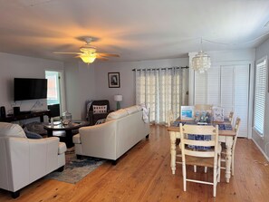 A living room with a ceiling fan, a TV, a sofa, a dining table with chairs, and a window with blinds. - Shucker's Tump -  pet friendly, Lg screened porch. LINENS AND TOWELS PROVIDED (Chincoteague)