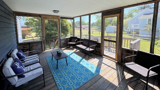 A covered porch with a seating area, a table, and a view of the surrounding area. - Shucker's Tump -  pet friendly, Lg screened porch. LINENS AND TOWELS PROVIDED (Chincoteague)