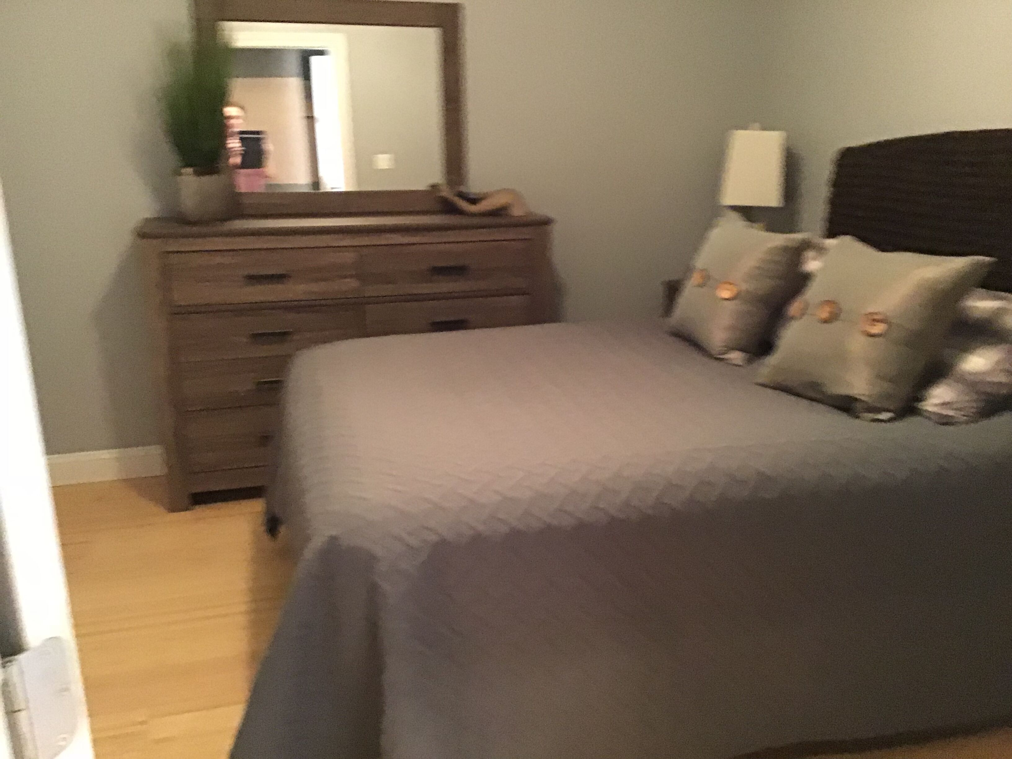 Une chambre à coucher avec un lit, une commode, un miroir et une lampe.