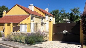 Une maison jaune avec un toit rouge, un mur en pierre et un portail en métal.