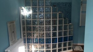 Une salle de bain avec un mur recouvert de carreaux bleus, une douche, une fenêtre et un plancher en bois.